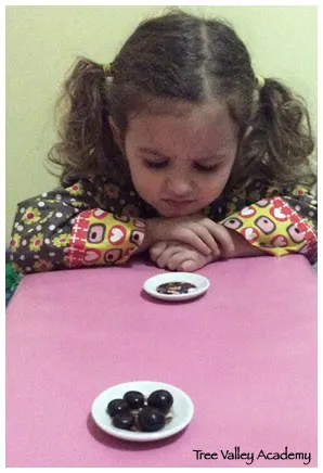 A young girl about 3 years old stares angrily at her empty plate. There's another plate of someone else's that has 5 candies.