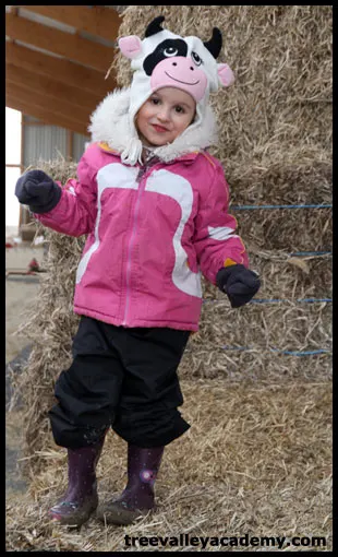 A girl playing on a haystack in a barn.