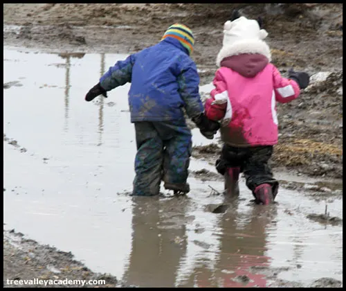 two children holding hands and walking through mud puddle