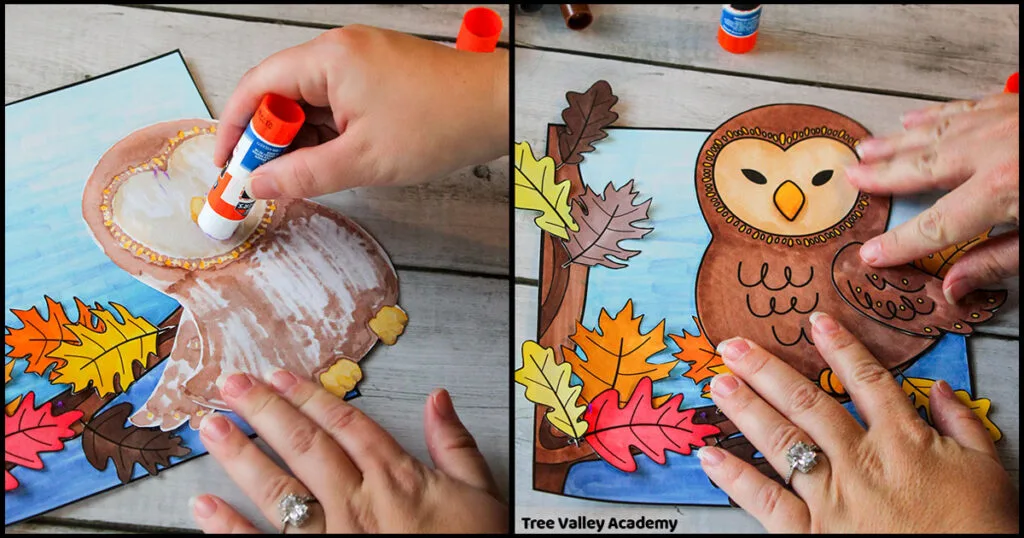 A person is using a glue stick to glue the back of the paper owl. Then they are pasting the owl in place so that it's standing on the branch of the oak tree.