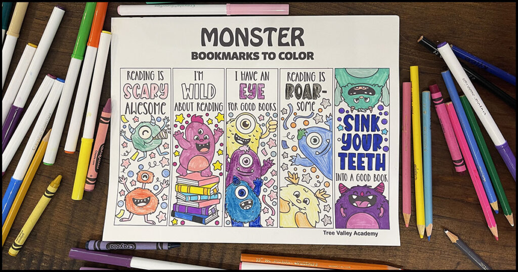 Colored monster bookmarks with fun reading sayings surrounded by crayons, markers, and pencil crayons on a wooden table.