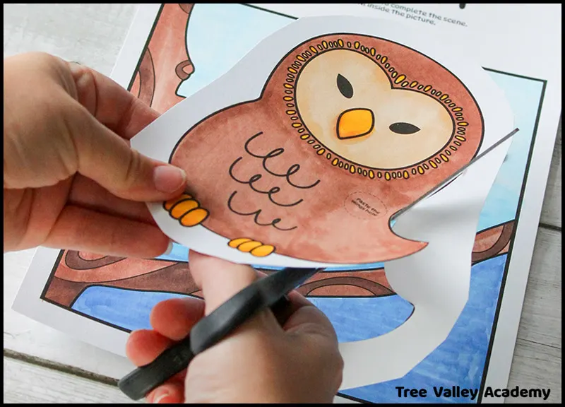 A child using scissors to cut out a picture of an owl that they had colored. This is a step in a kid's fall owl craft.