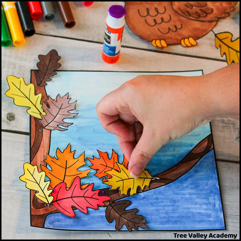 A fall owl craft for kids. In this step, a child is gluing colorful paper oak leaves to a tree coloring page.